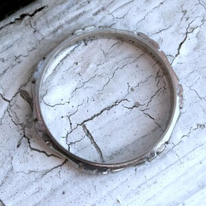 May include: A silver ring with a textured design. The ring is lying on a white, cracked surface.
