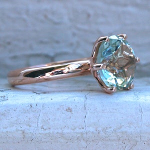 May include: A rose gold ring with a large, light blue gemstone set in a prong setting.