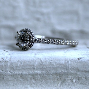 May include: A silver engagement ring with a round, clear center stone surrounded by smaller stones. The band is also set with small stones.