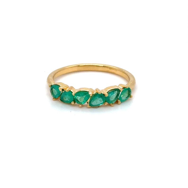 May include: A gold band ring with seven emerald green gemstones set in a row.