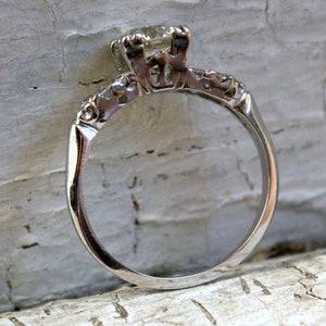 May include: A silver engagement ring with a single round diamond in a prong setting. The band is decorated with small diamonds.