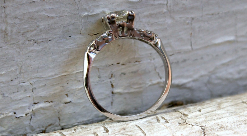 May include: A silver engagement ring with a single round diamond in a prong setting. The band is decorated with small diamonds.