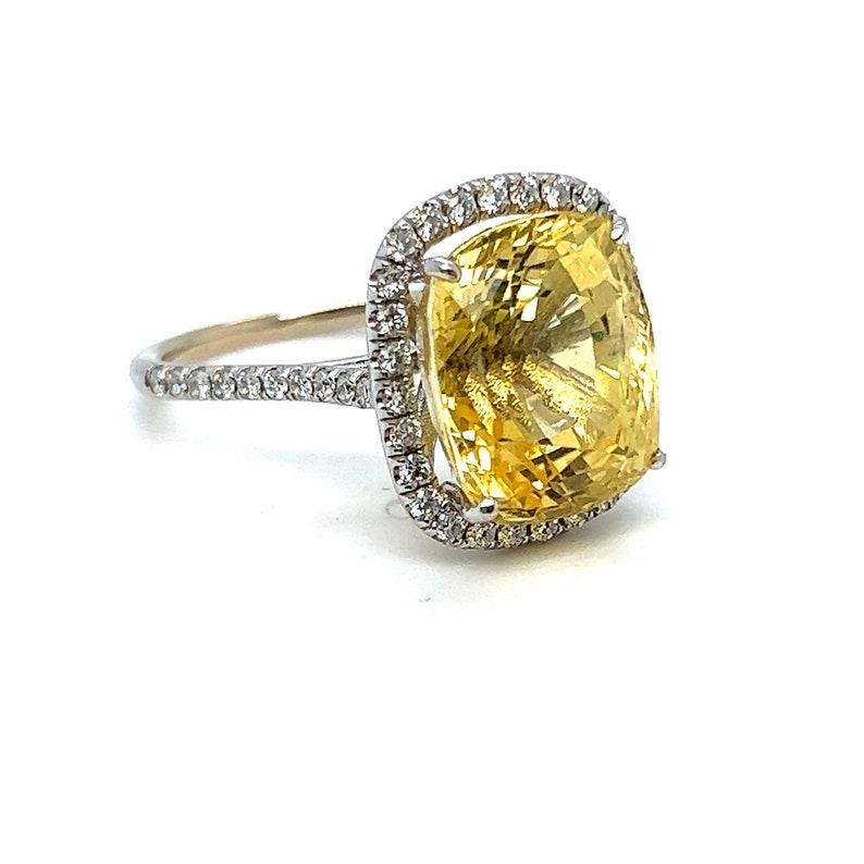 Op de afbeelding: Een opvallende ring met een grote, kussenvormige gele edelsteen, omringd door een halo van kleinere, sprankelende diamanten. De band is ook versierd met diamanten, wat een luxueus en opvallend sieraad cre&euml;ert.
