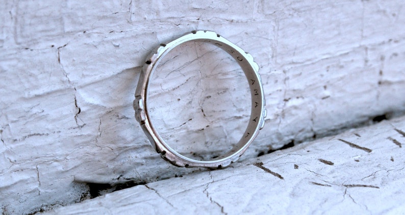 May include: A silver ring with a textured design and the word "OMAY" inscribed on the band.