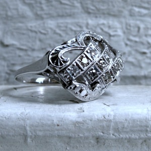 May include: A silver ring with a decorative design featuring a cluster of small diamonds.