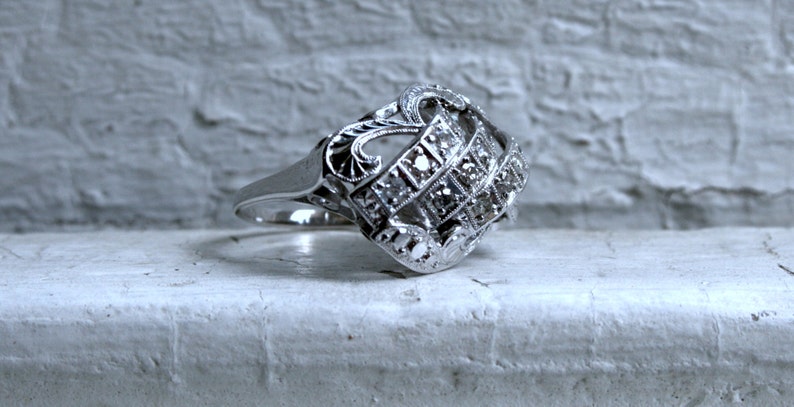 May include: A silver ring with a decorative design featuring a cluster of small diamonds.