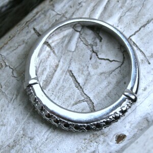 May include: A silver ring with a band of small black stones.