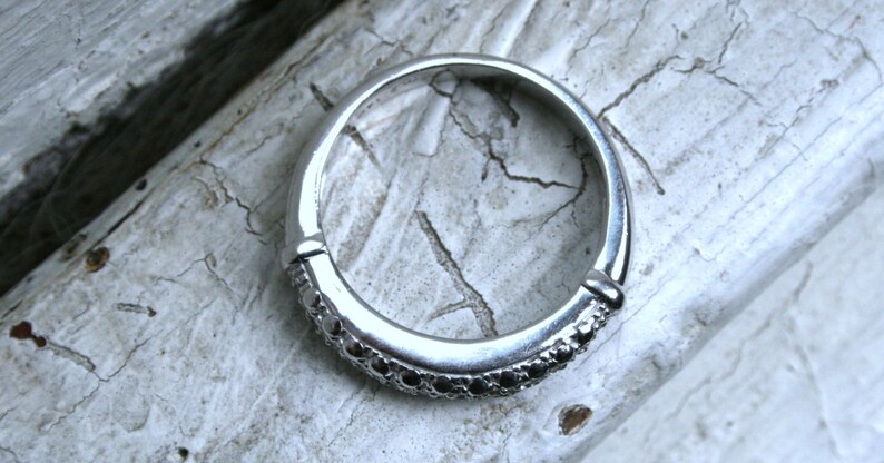 May include: A silver ring with a band of small black stones.