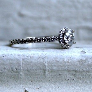 May include: A silver engagement ring with a large, round, clear diamond surrounded by smaller diamonds. The band is also set with small diamonds.