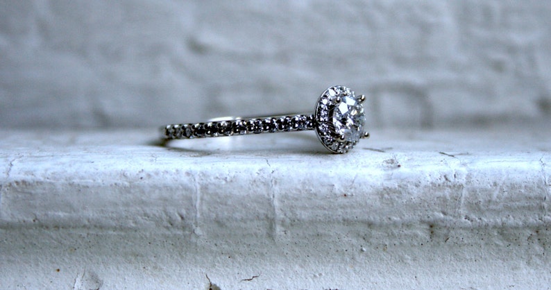 May include: A silver engagement ring with a large, round, clear diamond surrounded by smaller diamonds. The band is also set with small diamonds.