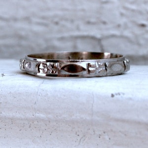 May include: A silver wedding band with a detailed, textured design. The band is smooth and shiny.