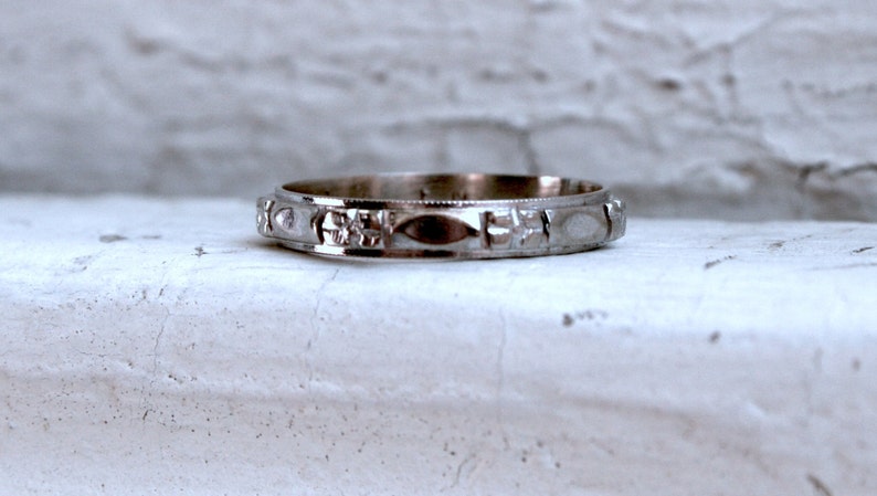 May include: A silver wedding band with a detailed, textured design. The band is smooth and shiny.