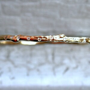 K&ouml;nnte beinhalten: Ein goldener Bandring mit einem strukturierten, ast&auml;hnlichen Design und kleinen Diamanten, die in die Oberfl&auml;che eingefasst sind.