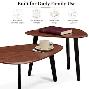 May include: Two nesting tables with dark wood-grain tops and black legs. The text Built for Daily Family Use appears above icons labeled Rounded Beveled Edges, Thermoformed Veneer, Solid Wood Legs, and Waterproof Surface. A book, cup, and spoon sit on top.