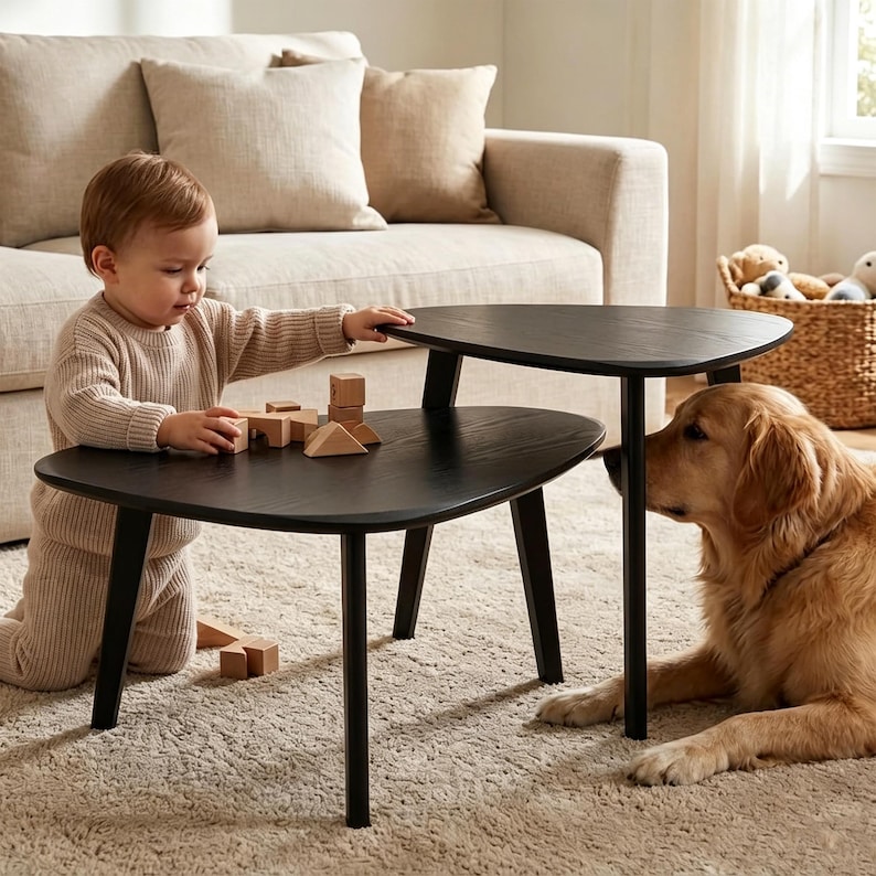 May include: A set of two black, triangular-shaped nesting tables with tapered legs. The tables feature a smooth, dark wood grain finish and are arranged at different heights, providing a functional surface for play and daily activities.