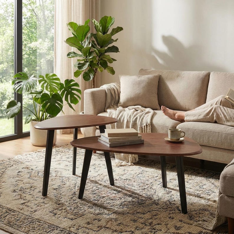 May include: A set of two nesting coffee tables with dark brown, kidney-shaped wooden tops and three tapered black metal legs each. The tables are arranged with one slightly overlapping the other, featuring a smooth finish and rounded edges.