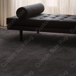 May include: A dark gray chaise lounge with a tufted seat and a cylindrical bolster pillow. The lounge has a minimalist design with a low profile and thin legs. The rug beneath is a matching dark gray color, creating a cohesive and modern aesthetic.
