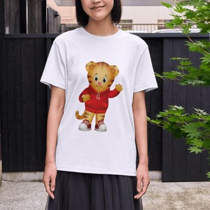 Op de afbeelding: Wit T-shirt met een cartoon tijger met een rode hoodie en sneakers. De tijger zwaait met zijn hand. Het shirt heeft een ronde hals en is gemaakt van zacht materiaal.