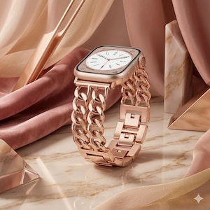 May include: Rose gold smartwatch with a chain link band. The watch face is white with black hands and numerals. The band is made of interlocking links. The watch is displayed on a marble surface with pink fabric and geometric shapes in the background.