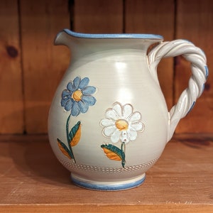 May include: A white ceramic pitcher with a blue and white floral design. The pitcher has a twisted handle and a blue rim.