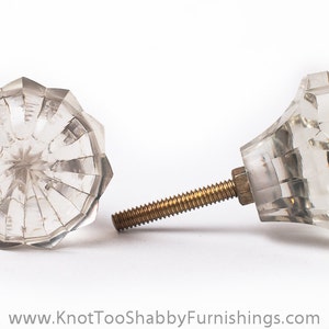 May include: Two clear glass cabinet knobs with a faceted design. The knobs have a brass screw.