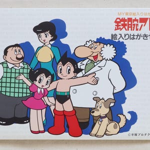 May include: A postcard featuring a group of cartoon characters, including a robot boy in red boots and a dog. The characters are set against a white background with Japanese text at the top.