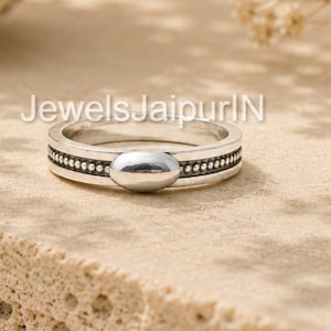 May include: A silver ring with an oval center stone and a dotted border. The ring is displayed on a textured, light-colored surface. The text "JewelsJaipurIN" is visible in the image.