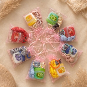 May include: A selection of small gift bags, each containing lip balm, scrunchies, and jewellery. The lip balms are in various colours, including orange, green, and red. The scrunchies and jewellery are in coordinating colours.