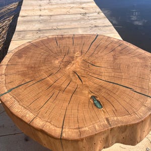 Puede incluir: Una mesa de centro redonda de madera natural con acabado marrón claro. La mesa tiene un borde natural y veta de madera visible. Resina azul oscuro rellena las grietas. La mesa tiene unos 76 cm de diámetro.