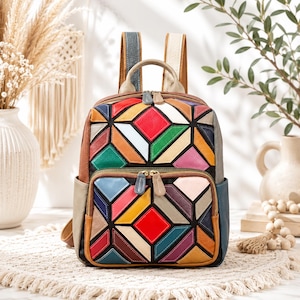 May include: A leather backpack featuring a geometric patchwork design in vibrant colors including red, green, yellow, blue, and pink. The bag has a top handle, two shoulder straps, a main zippered compartment, and a smaller front zippered pocket.