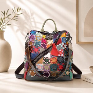 May include: A colorful patchwork leather backpack with a floral design. The bag features a top handle, adjustable straps, and a zippered closure. The design incorporates various colors and textures, with a red tassel accent.