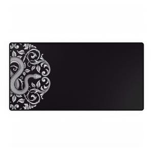 Peut inclure: Tapis de bureau rectangulaire noir avec un motif orné détaillé sur le côté gauche. Le motif comprend un serpent enroulé avec des feuilles et des éléments floraux tourbillonnants en gris et blanc. Le reste du tapis est noir uni. Environ 70 cm de long.
