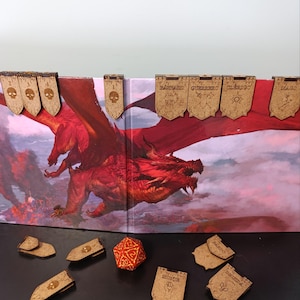 Puede incluir: Accesorios de juego de madera con una ilustración de dragón rojo. Incluye pancartas de madera con texto, fichas con forma de calavera y un dado de veinte caras rojo y blanco. Las pancartas tienen texto en español.