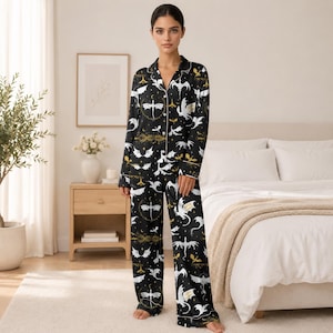 May include: Black pajama set with a dragon pattern. The long-sleeved top and pants feature a repeating design of white and gold dragons, stars, and celestial elements against a black background. The pajamas have white trim.