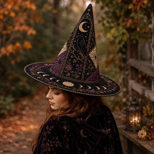 May include: A pointed witch hat in black, featuring intricate gold and purple embroidery of a raven, crescent moon, spiderwebs, and floral motifs. The wide brim displays a sequence of moon phases in gold thread against a dark fabric background.