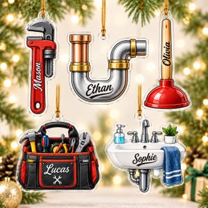 May include: Five acrylic ornaments featuring plumbing and tool themes: a red pipe wrench labeled Mason, a silver U-pipe labeled Ethan, a red plunger labeled Olivia, a black and red tool bag labeled Lucas, and a white sink labeled Sophie.