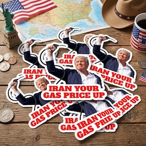 May include: A collection of stickers featuring a man holding a gas pump nozzle, with the text "IRAN YOUR GAS PRICE UP" in red. The stickers are scattered on a wooden surface, alongside an American flag, a map, and a cowboy hat.