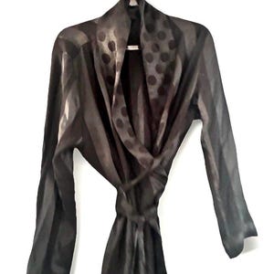 May include: A black robe with a striped pattern and a polka dot collar. The robe has long sleeves and a tie belt. The robe is hanging on a white background.