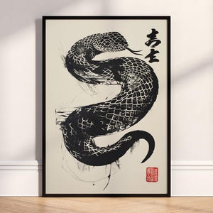 May include: Framed art print featuring a black and white snake illustration. The artwork, in a brushstroke style, includes Japanese characters and a red stamp. The print is set against a cream background within a black frame.