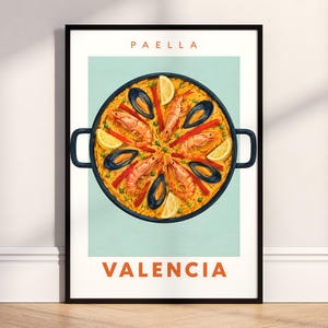 May include: A framed vertical poster featuring a centered illustration of a black paella pan filled with yellow rice, shrimp, mussels, red pepper strips, green peas, and lemon wedges. The text "PAELLA" appears at the top and "VALENCIA" at the bottom.