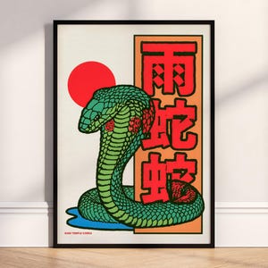 May include: Framed art print depicting a green cobra with red details, set against a red sun and orange background. Red Japanese characters are displayed. The text "Rain Temple Cobra" is at the bottom of the print.