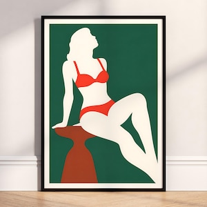 May include: A framed wall art print featuring a minimalist graphic illustration of a cream-coloured silhouette of a person wearing a bright red bikini, sitting on a brown stool against a solid dark green background with a thin white border.