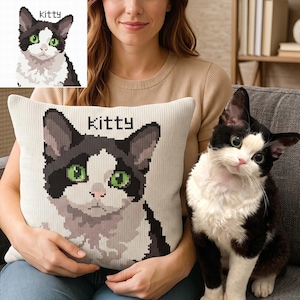 May include: A square throw cushion featuring a knitted graphic of a black and white cat with bright green eyes and the word "Kitty" printed above its head. The design mimics a pixelated pattern, showcasing the cat's face and chest in detail.