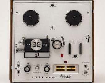 May include: Vintage Akai X-150D solid state custom deck tape recorder. The silver face has black reels, knobs, and switches. The wooden side panels frame the device. The text "AKAI SOLID STATE" and "Custom Deck X-150D" are visible.