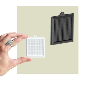 May include: Two square pegboard-style display panels, one white and one black, each featuring a grid of small holes and a small tab with a hole at the top for hanging. The white panel is held up, while the black panel is positioned to the right.