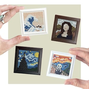 May include: Four miniature square cross-stitch artworks framed in small white and dark brown frames. The designs depict famous paintings including The Great Wave, the Mona Lisa, The Starry Night, and The Scream, rendered in pixelated embroidery.