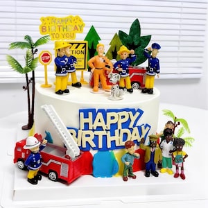 May include: A birthday cake decorated with a firefighter theme. The white cake has blue lettering that reads "Happy Birthday". It is decorated with toy fire engines, firefighters, a Dalmatian, and miniature palm trees.