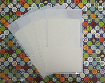 May include: A stack of off-white cardstock cards inside clear cellophane sleeves. The cards are rectangular with rounded corners. The background is a dark blue fabric with a pattern of colorful circles.