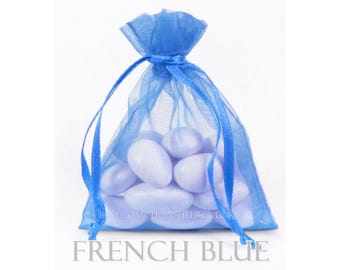 May include: A bright blue sheer organza drawstring pouch filled with several smooth, oval-shaped white candies. The bag is cinched at the top with matching blue ribbon ties, creating a gathered effect. The text FRENCH BLUE is printed below.