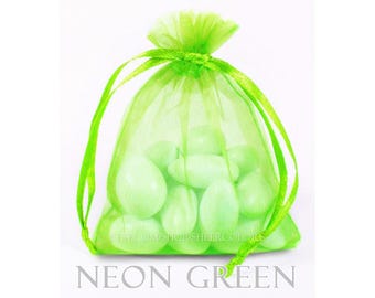 May include: A neon green organza drawstring bag filled with several smooth, light green oval-shaped candies. The bag is made of a sheer, semi-transparent fabric and is cinched at the top with matching neon green ribbon ties. The text NEON GREEN is visible.
